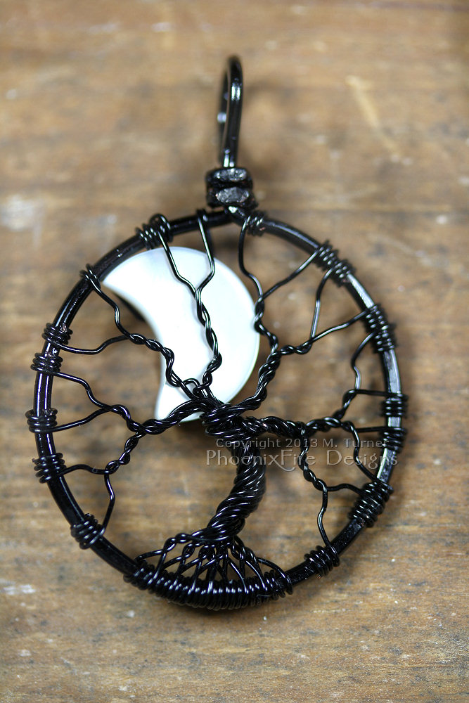 A mother of pearl crescent moon peeks out from behind the black wire branches of this handmade wire wrapped tree of life pendant like a lunar eclipse in the night sky.