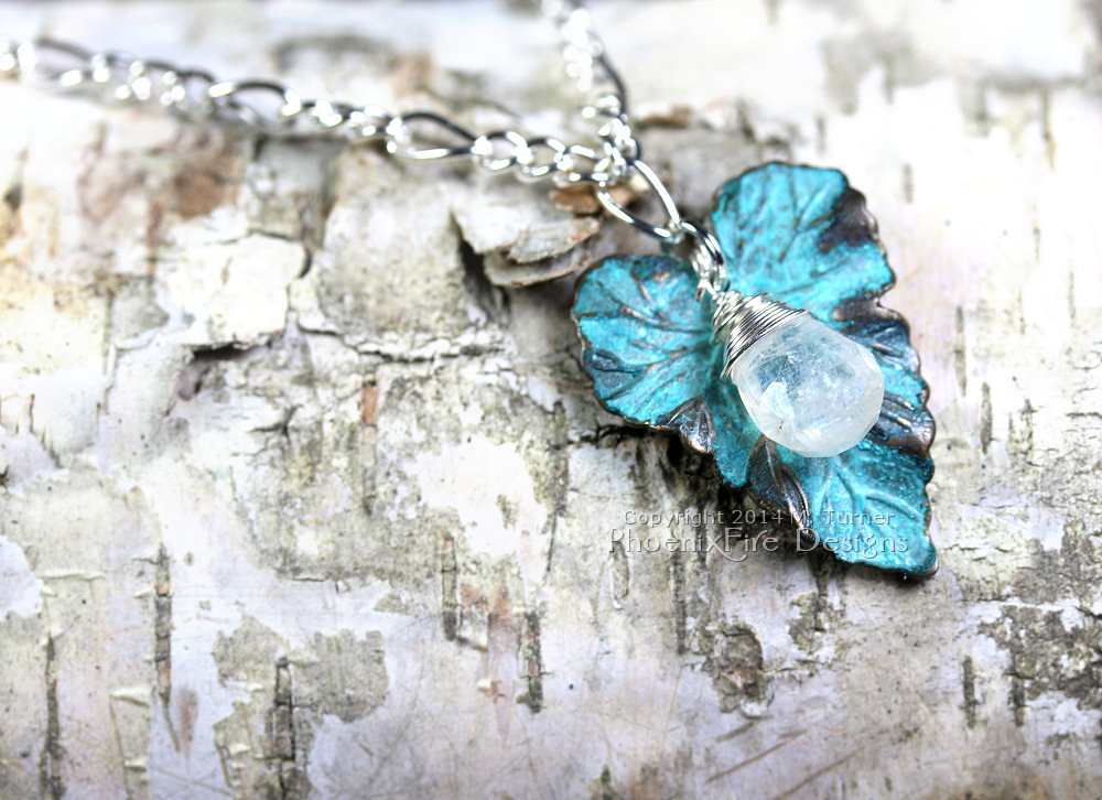Glowing blue micro-faceted Rainbow Moonstone Briolette is nestled on a verdigris patina brass leaf charm. On a sterling silver plated chain of 18 inches.