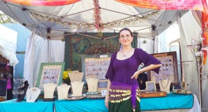 Handmade jewelry designer and wire wrapped tree of life artist, Miss M. Turner of PhoenixFire Designs standing in front of her craft show booth display at the Bay Area Renaissance Festival in Gypsy style costume, long skirts, belly dance skirt, coin belt, peasant blouse, boho style.