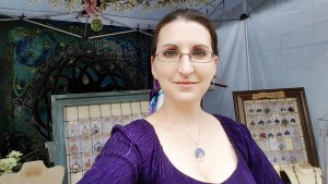 Handmade jewelry designer and wire wrapped tree of life artist, Miss M. Turner of PhoenixFire Designs standing in front of her craft show booth display at the Bay Area Renaissance Festival in Gypsy style costume, long skirts, belly dance skirt, coin belt, peasant blouse, boho style.